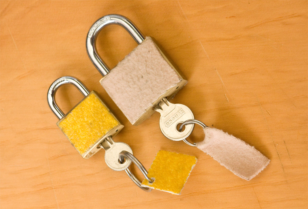 Pictured are two padlocks with keys in them. The left padlock is covered in velcro and the key has a velcro tag. The right padlock is covered in soft felt and has a soft felt tag.