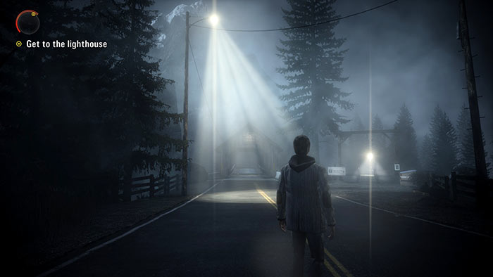 A screenshot of the videogame Alan Wake. The main character stands in the middle of a road at night. A streetlight casts an inviting pool of light – and up ahead a light on a building in the distance tells the player where to go next.